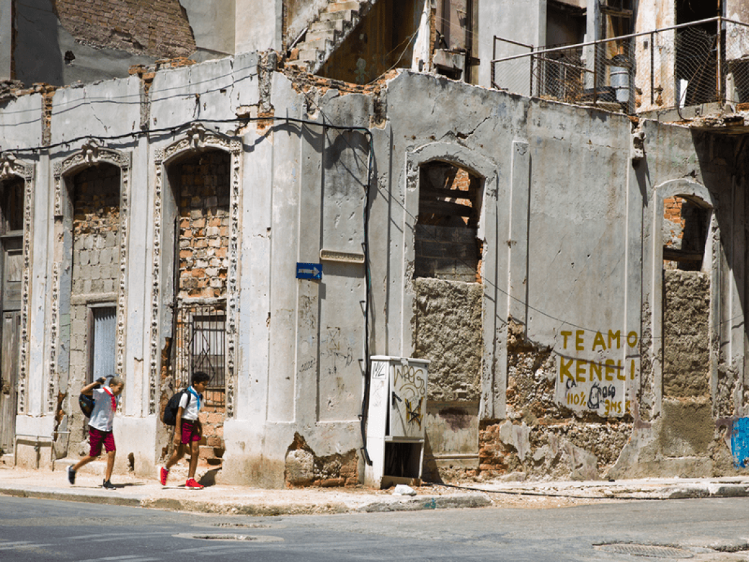 Niños caminan a la escuela entre edificios en ruinas.