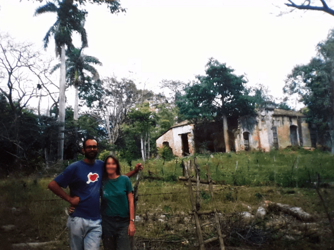 Dos personas posando en el campo cubano. Detrás, las ruinas de una casa antigua.