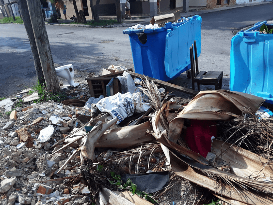 Contenedores de basura rotos y desbordados de desperdicios en la calle.