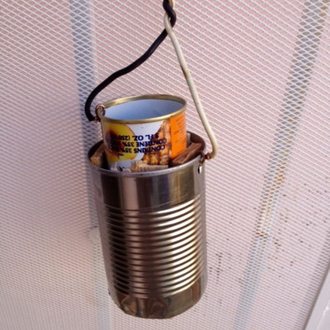 Calentador de agua casero hecho con dos latas encajadas y cables eléctricos, colgado de un gancho.