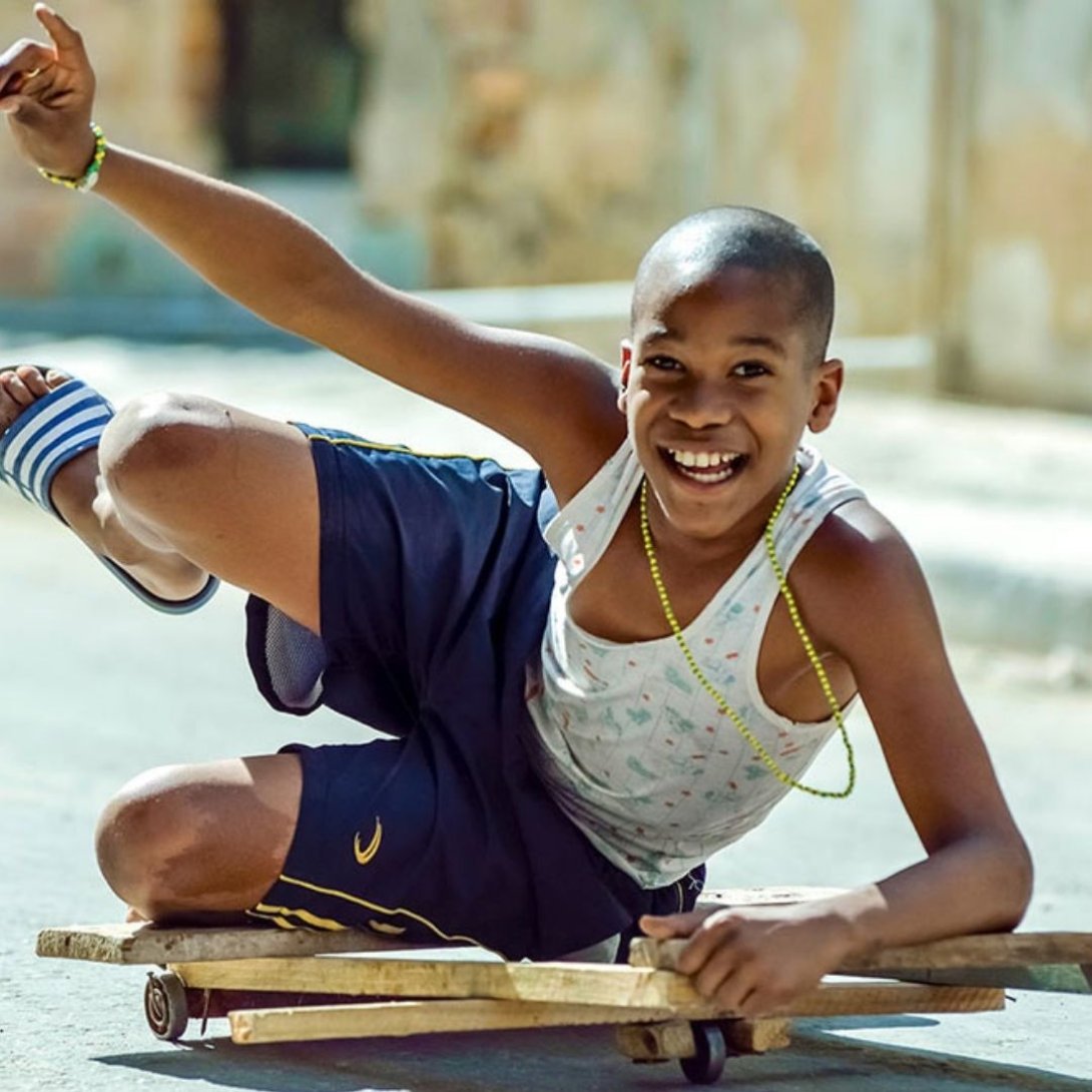 Niño sonriente desliza una chivichana de madera con ruedas por la calle.