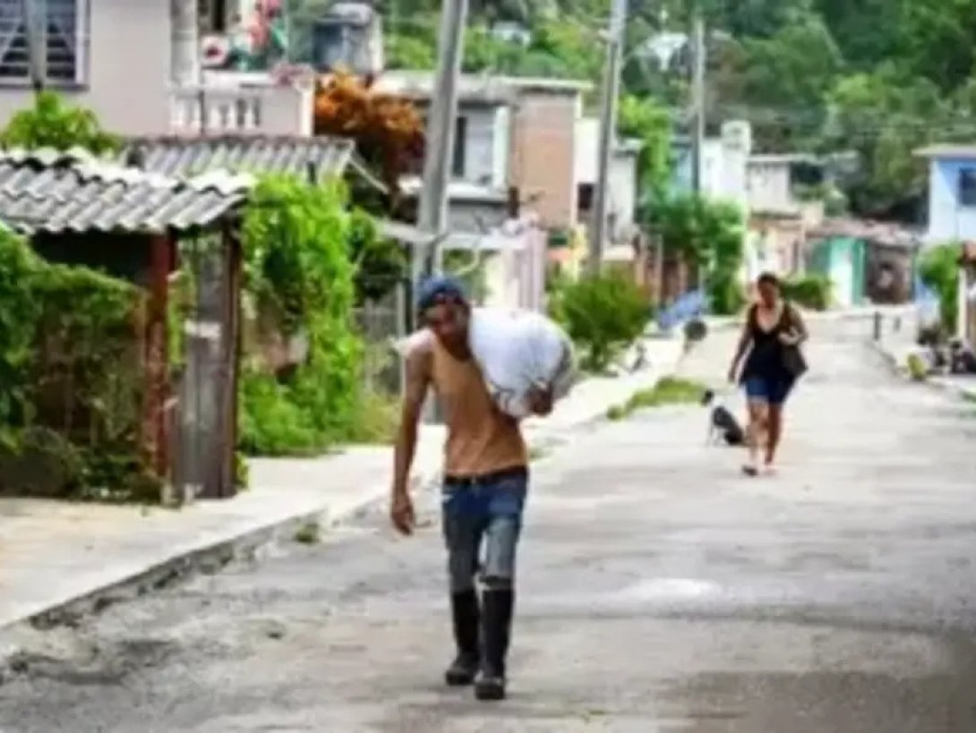 Persona cargando un saco al hombro por una calle de un barrio en Cuba.