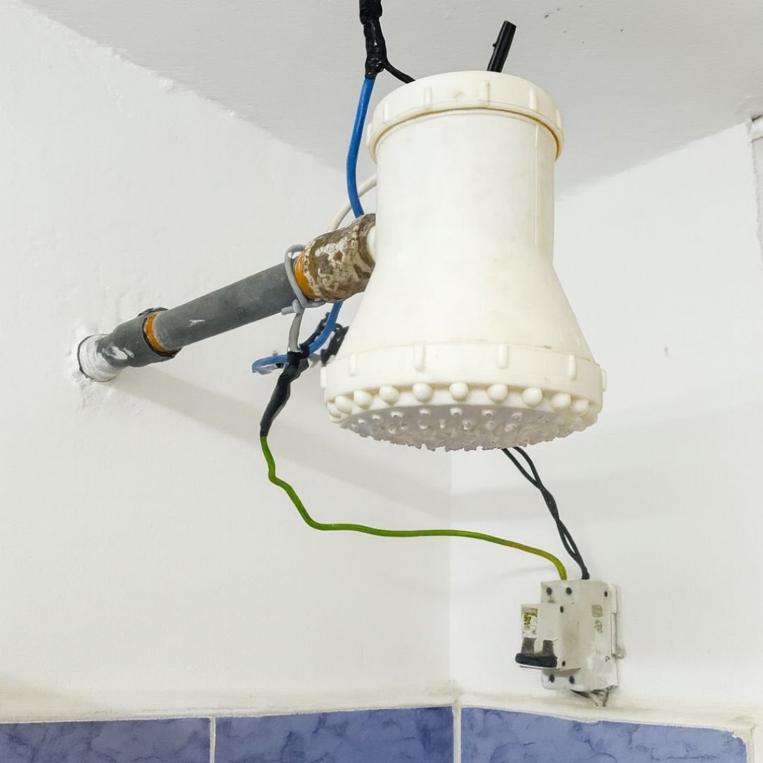 Cabezal de ducha improvisado con cables expuestos y resistencia eléctrica, instalado en un baño.