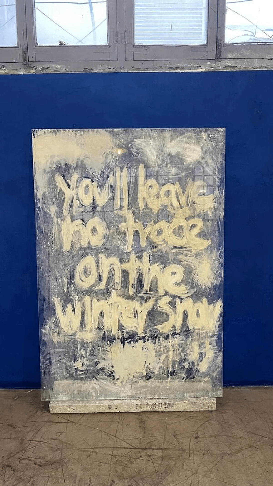Instalación de cristal y concreto donde se lee: "You'll leave no trace on the winter snow".