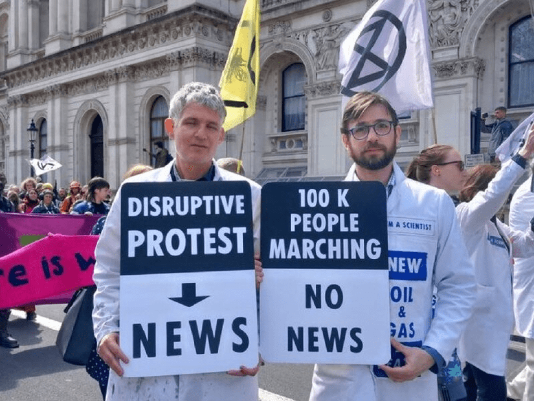 Dos científicos sosteniendo carteles que alertan cómo las protestas disruptivas estuvieron en los medios pero más de 100 mil personas manifestándose, no.