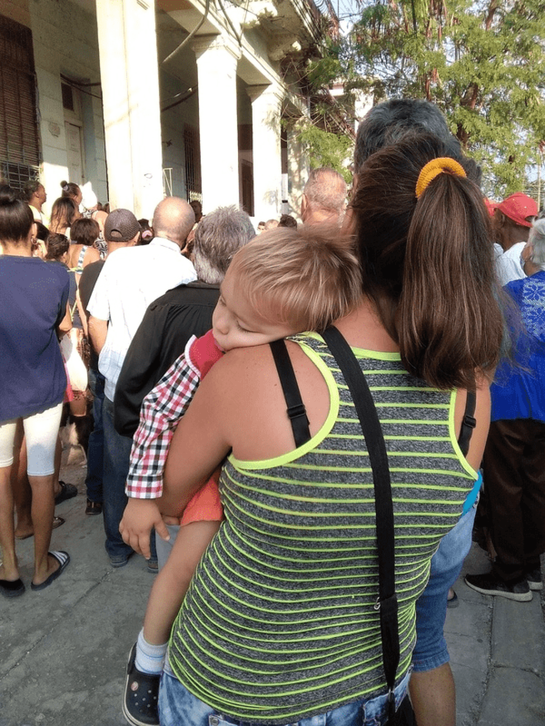 Mujer con un niño en brazos en una cola en Cuba.