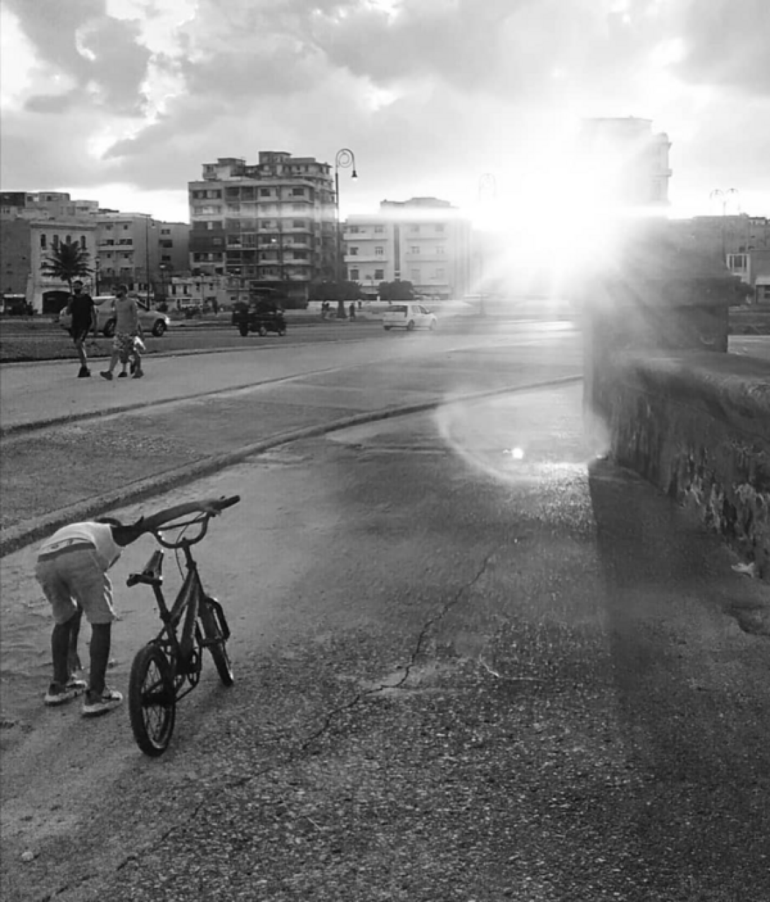 Vista del malecón habanero con transeúntes: un niño con su bicicleta, al fondo el sol.