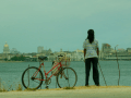 Mujer de espaldas y al lado de una bicicleta mira a La Habana detrás del mar.