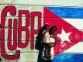 Mujer cargando una niña frente a una pared con la bandera cubana