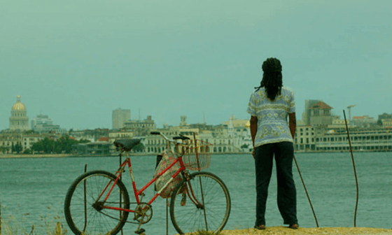 Mujer de espaldas y al lado de una bicicleta mira a La Habana detrás del mar.