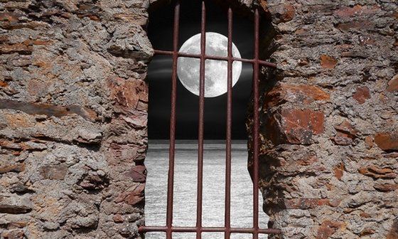 Una luna llena sobre el mar a través de las rejas de una cárcel.