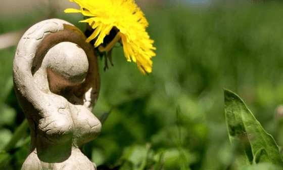 Figura de una diosa pagana con una flor en la yerba.