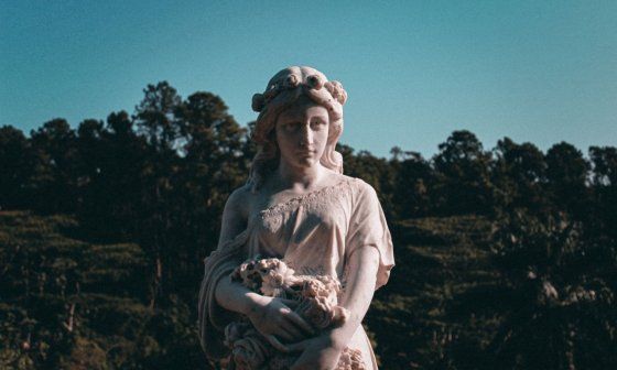 Estatua de mujer con flores en brazos.