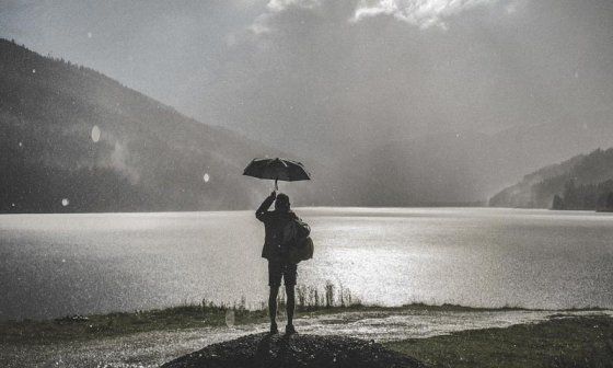 Mujer con sombrilla de frente a un lago mientras llueve.