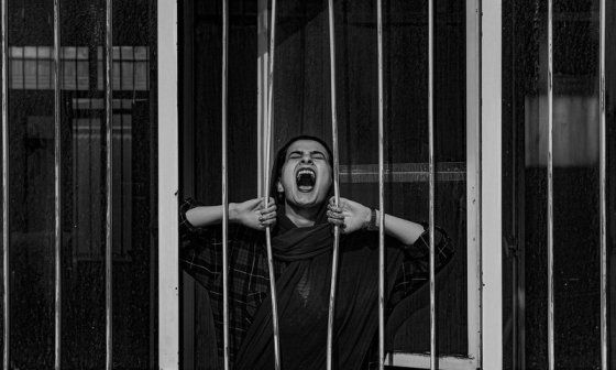Mujer gritando mientras abre los barrotes de una reja.