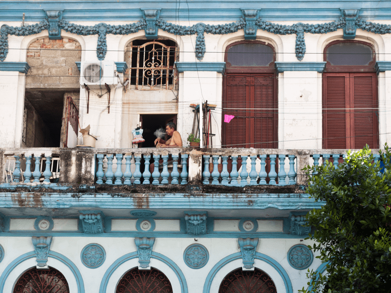 Hombre fumando en un balcón de un viejo edificio.