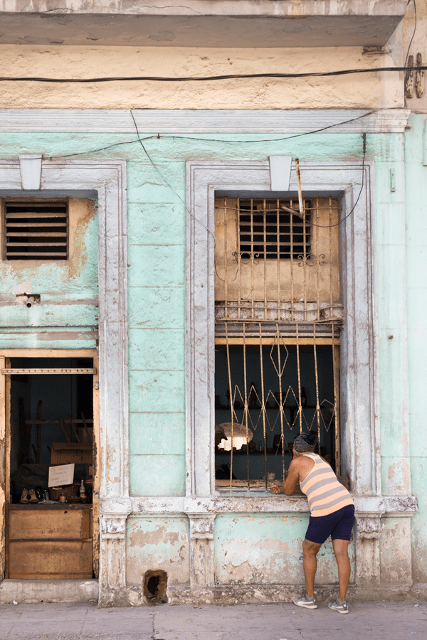 Mujer recostada en la acera a una ventana. |  Imagen:  Alina Sardiñas