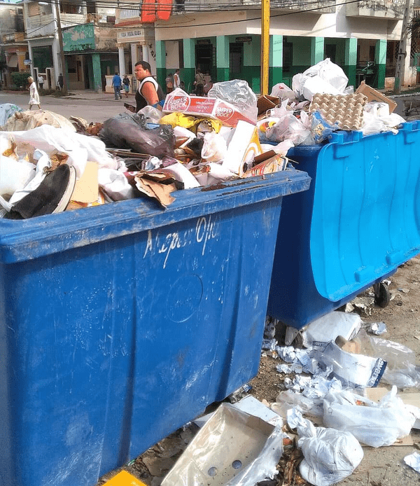 Dos contenedores azules de basura desbordan desperdicios hacia la calle.  |  Imagen:  Alberto Garrandés